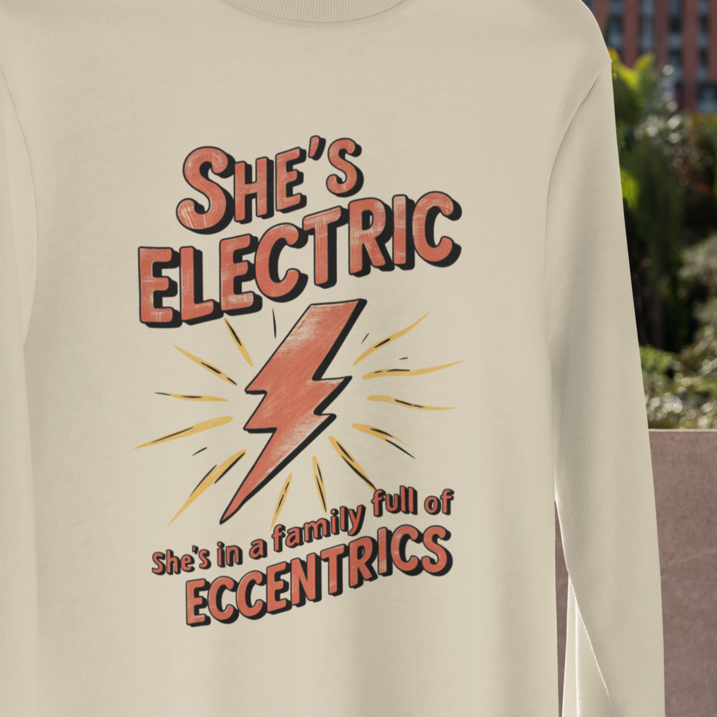 Vibrant graphic tee featuring the iconic phrase 'She's Electric, She's in a family full of eccentrics' against a colorful background, perfect for fans of Oasis and those who embrace individuality."